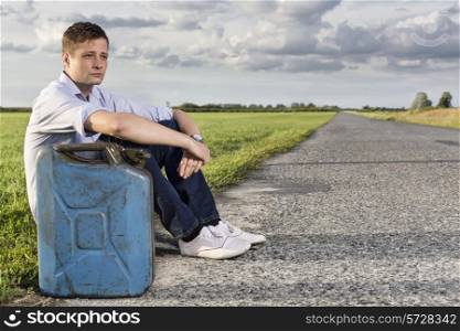 Full length of young man with empty gas can sitting by road