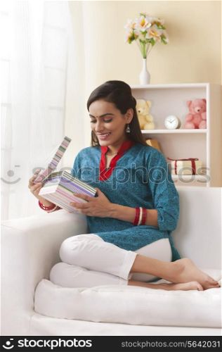 Full length of young married Indian woman opening gift box in living room