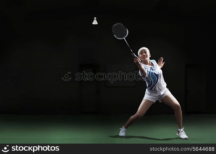 Full length of young woman hitting shuttlecock with badminton racket at court