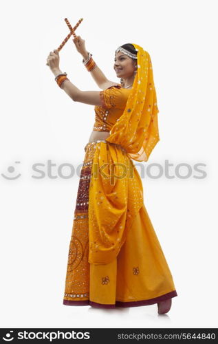 Full length of young woman in chaniya choli performing Dandiya Raas over white background