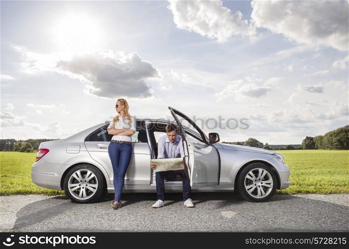 Full length of young woman looking away while man reading map in car at countryside