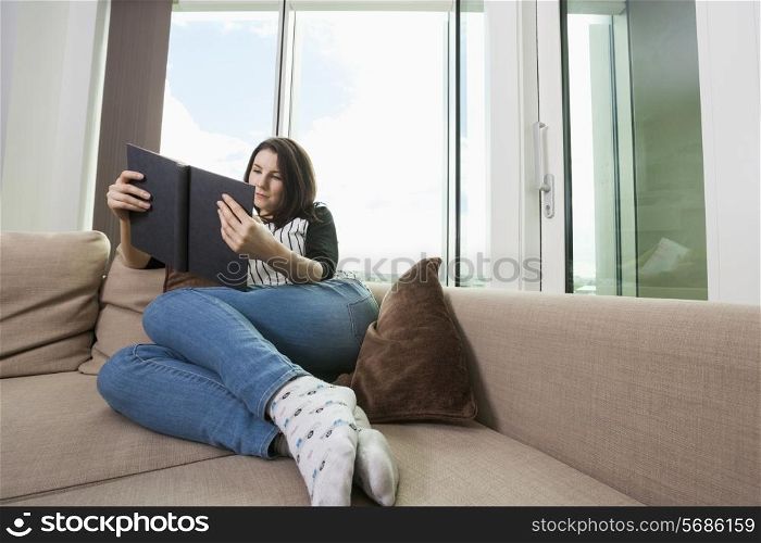 Full length of young woman reading book on sofa