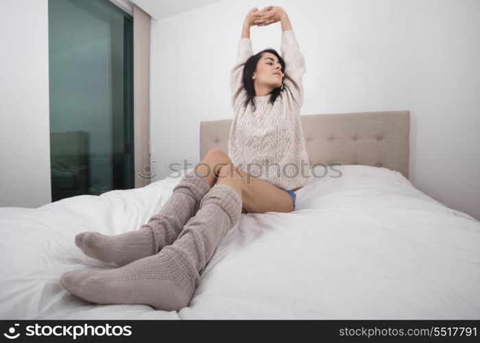 Full length of young woman stretching in bed