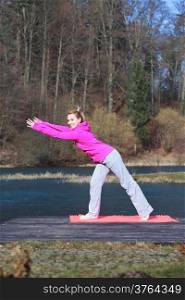 Full length of young woman teenage girl in pink tracksuit doing morning exercise on mat on pier outdoor. Healthy active lifestyle.