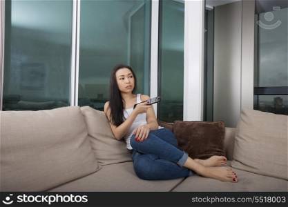 Full length of young woman watching TV in living room