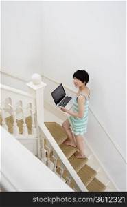 Full length of young woman with laptop walking up stairway
