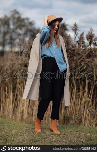 Full length outdoor portrait of beautiful young woman with long straight hair. Model dressed in coat, shirt and hat.. Full length outdoor portrait of beautiful young woman with long straight hair. Model dressed in coat, shirt and hat
