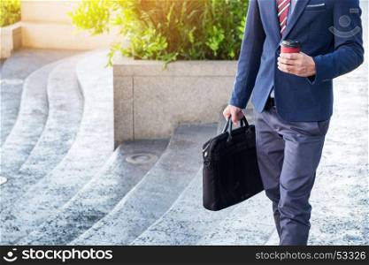 full length picture of a young business man walking forward with a briefcase in one of his hands and coffee cup.