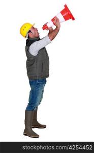 full-length picture of builder in profile shouting in construction cone