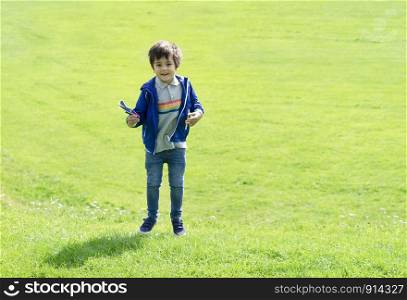 Full length portrait kid jumping in the green grass, Cute little boy playing plastic airplane toy, Child having fun playing outdoor in spring or summer field on sunny day.