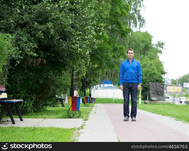 Full-length portrait of a young middle-aged man in a blue jacket and jeans, standing silently in the summer park
