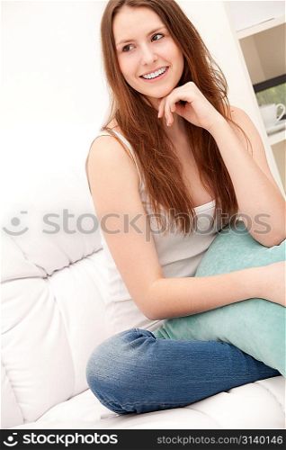 Full-length portrait of a young woman hugging her pillow sitting on sofa