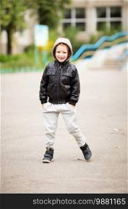 Full-length portrait of adorable little boy wearing black leather jacket. Urban kids. Hands in pockets. Loss of primary teeth in children.