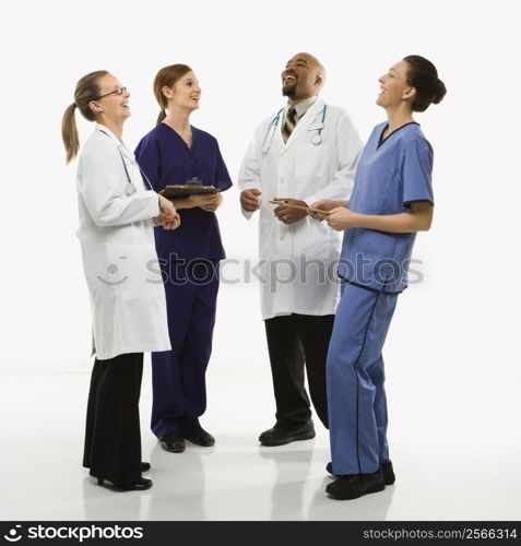 Full-length portrait of African-American man and Caucasian women medical healthcare workers in uniforms laughing standing against white background.