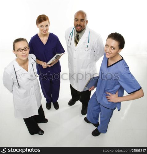 Full-length portrait of African-American man and Caucasian women medical healthcare workers smiling in uniforms standing against white background.
