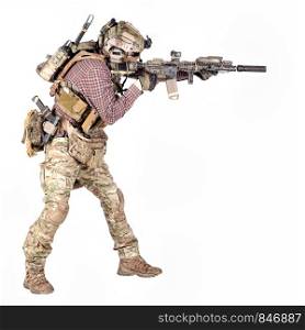 Full length portrait of airsoft player in checkered shirt, wearing camouflage uniform, helmet with tactical radio headset, body armour, aiming with service rifle replica studio shoot isolated on white. Airsoft player aiming service rifle studio shoot