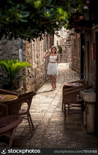 Full length portrait of beautiful woman standing in shadow of big tree at narrow street