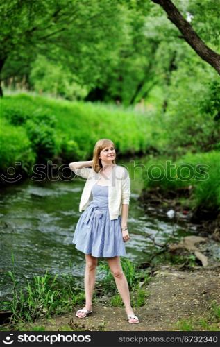 Full length portrait of beautiful young blond woman posing outdoors on river bank