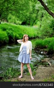 Full length portrait of beautiful young blond woman posing outdoors on river bank
