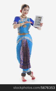 Full length portrait of Bharatanatyam dancer showing web page on digital tablet on while background