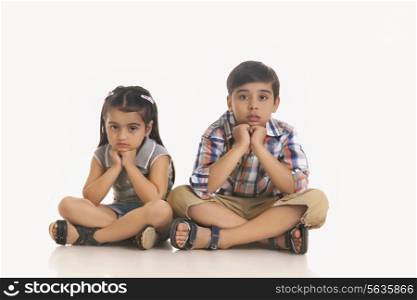 Full length portrait of bored siblings sitting against white background