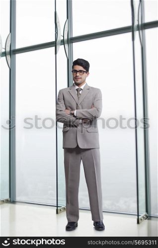 Full length portrait of businessman standing arms crossed in office