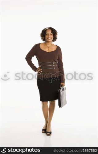 Full length portrait of businesswoman standing with hand on hip holding briefcase.