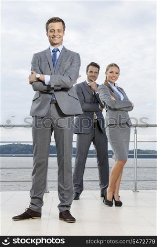 Full length portrait of confident businessman standing with coworkers on terrace against sky