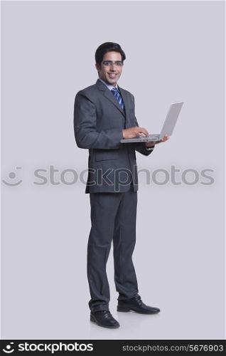 Full length portrait of confident businessman using laptop against gray background