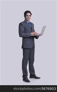 Full length portrait of confident businessman using laptop against gray background