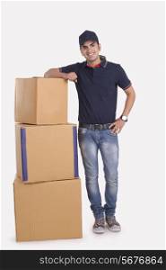 Full length portrait of confident delivery man with stacked packages against white background