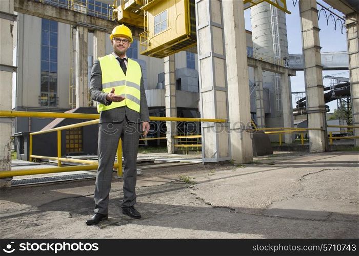 Full length portrait of confident male engineer gesturing outside industry