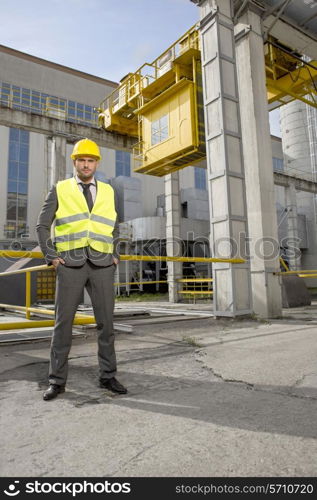 Full length portrait of confident young male engineer standing outside industry