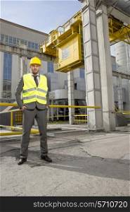 Full length portrait of confident young male engineer standing outside industry