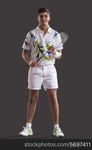 Full length portrait of confident young man with tennis racket standing isolated over gray background