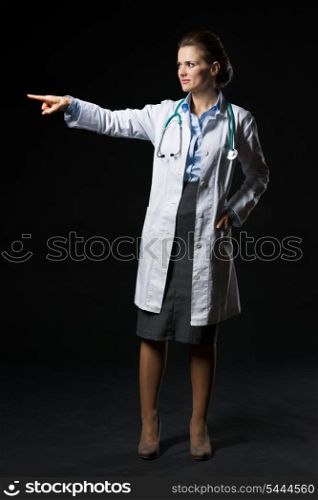 Full length portrait of doctor woman pointing on copy space isolated on black