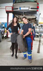 Full length portrait of female customer and mechanic holding tire in hand