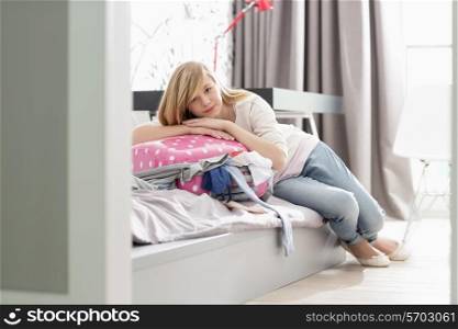 Full-length portrait of girl relaxing on bulging suitcase at home