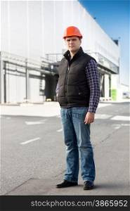 Full length portrait of handsome engineer posing against big warehouse