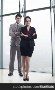 Full length portrait of happy business colleagues standing arms crossed in office