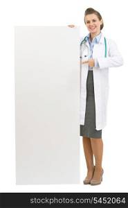 Full length portrait of happy doctor woman pointing on blank billboard