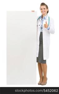 Full length portrait of happy doctor woman showing blank billboard and thumbs up