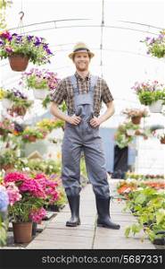 Full-length portrait of happy gardener standing at greenhouse