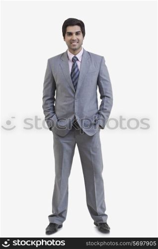 Full length portrait of happy young businessman with hands in pockets standing against white background