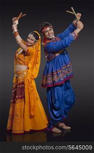 Full length portrait of happy young Indian couple performing Dandiya Raas over black background