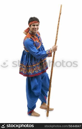 Full length portrait of happy young man in traditional wear holding stick isolated over white background