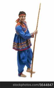 Full length portrait of happy young man in traditional wear holding stick isolated over white background
