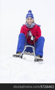 Full length portrait of happy young woman enjoying sled ride in snow