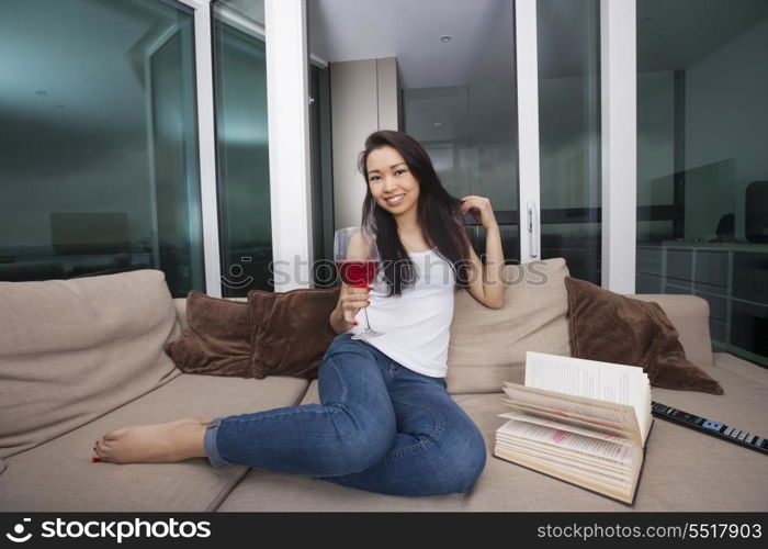 Full length portrait of happy young woman having red wine in living room