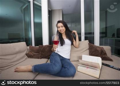 Full length portrait of happy young woman having red wine in living room